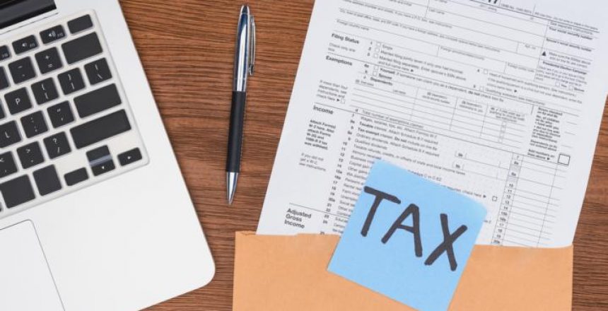 top view of tax form, laptop and blue card with 'tax' word at workplace תזכיר חוק מיסוי