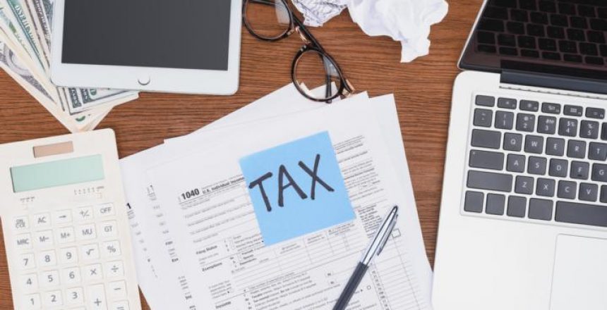 top view of tax forms, digital devices and blue card with 'tax' word on desk מחשבון מס שבח